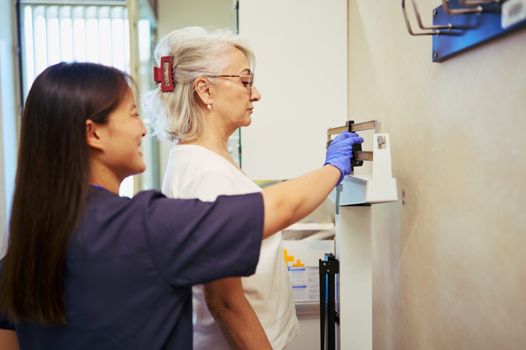 Nurse measuring patient weight on medical scale in hospital